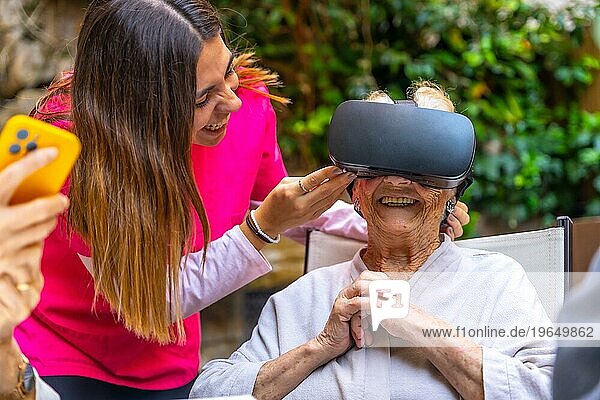 Krankenschwester  die eine ältere Frau mit einer Virtual Reality Brille in einer geriatrischen Einrichtung betreut