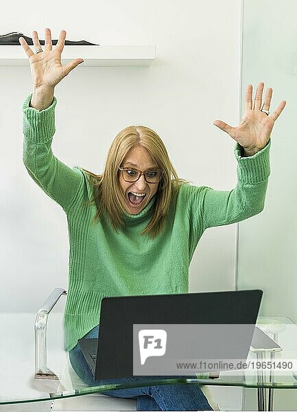 Porträt einer aufgeregten Frau im mittleren Erwachsenenalter  die ihren Erfolg feiert und die Arme hebt  während sie einen Laptop benutzt. Konzept gewinnen