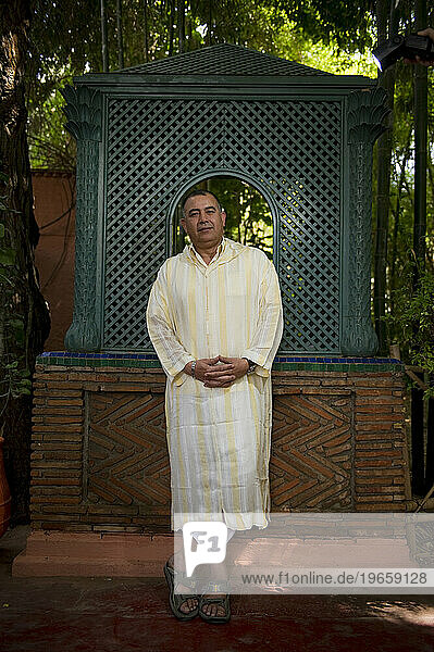 A man wearing traditional Middle Eastern dress stands in a Moroccan garden.