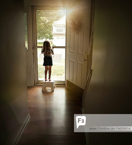 Toddler standing on stool looking out home window