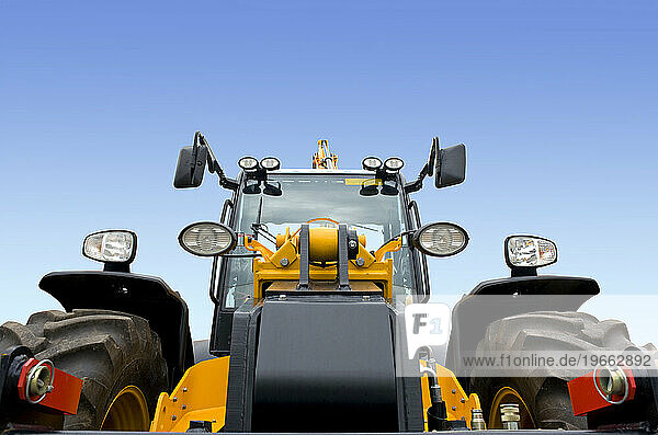 A frontal view of a new modern earth digger vehicle with yellow paint and a driver cab.