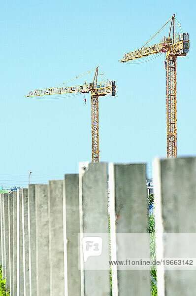 Two construction cranes above a row of concrete pillars