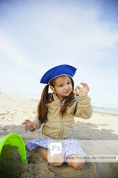 A cute little hispanic girl looks at a small seashell while playing in the sand.