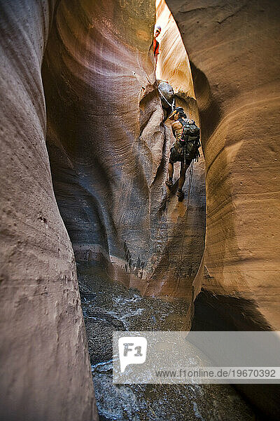 A woman rappelling into filthy pool in slot canyon  Utah.