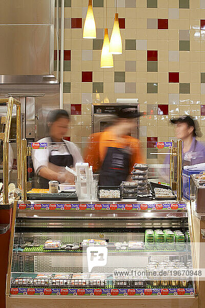 Three employees (blurred) working behind the counter at an eatery in a grocery store.