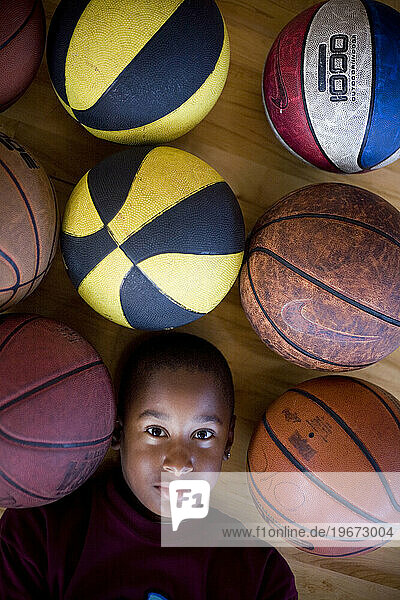 A young boy lies amongst a group of basketballs.