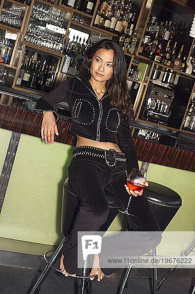 A woman sits at a bar with a drink.