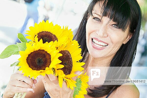 Fröhliche brünette Frau hält einen frisch geschnittenen Sonnenblumenstrauß auf dem Bauernmarkt