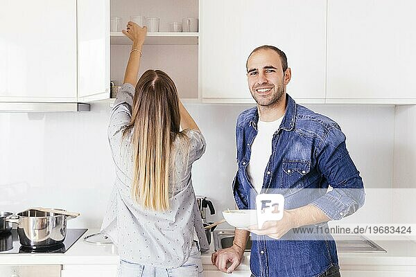 Porträt lächelnd junger Mann hält Schüssel Hände stehen in der Nähe seiner Frau Küche