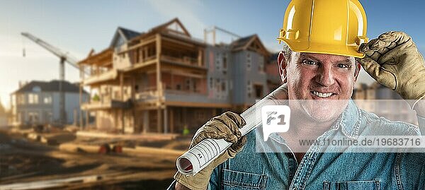 Freundlicher männlicher Bauunternehmer auf einer Baustelle mit Schutzhelm und Arbeitshandschuhen  der seine Baupläne hält
