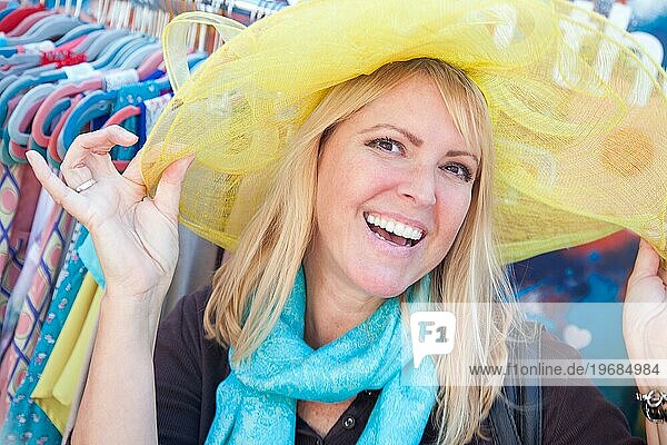 Glückliche blonde Frau modelliert spielerisch einen großen Sonnenhut auf dem Markt