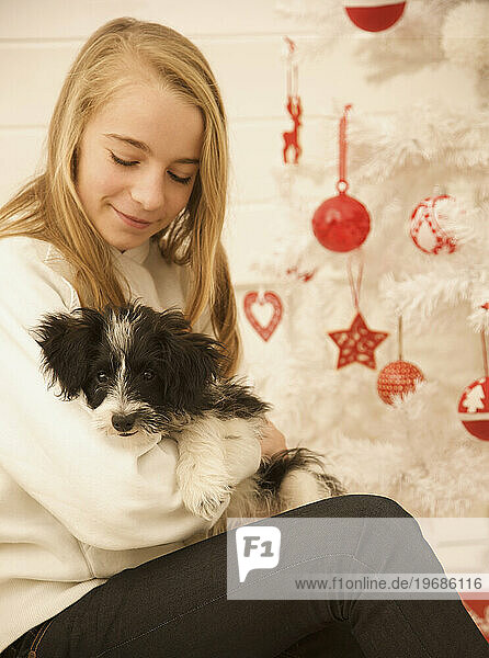 Young girl sitting by a Christmas tree holding a puppy
