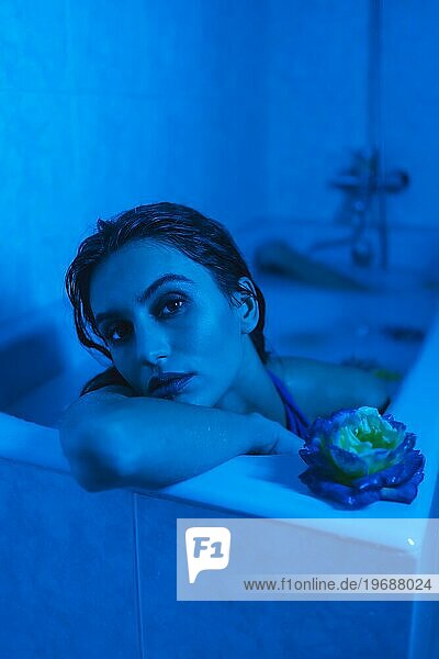 Vertikale künstlerische Porträt mit blauen Lichtern von einer sinnlichen Frau in einer entspannenden Momente in einem heißen Rohr