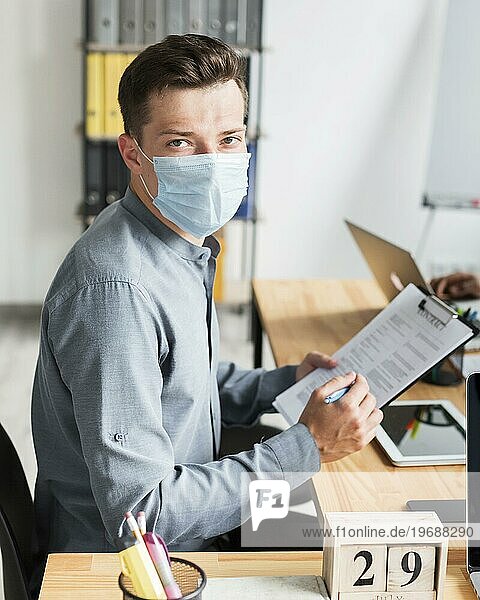Mann mit Maske arbeitet während der Pandemie im Büro