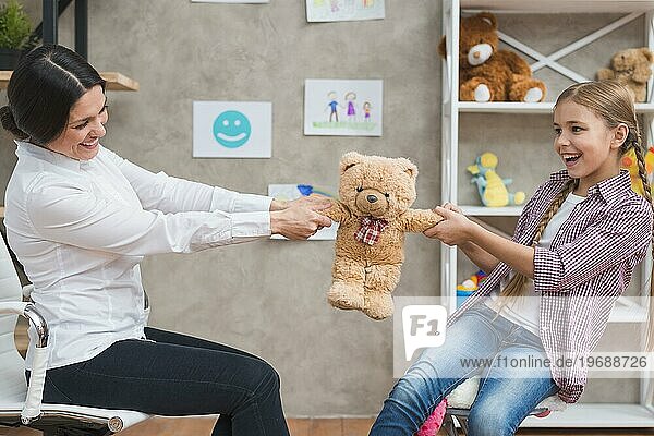 Weiblicher Psychologe lächelndes Mädchen sitzend Gesicht Gesicht ziehen Teddybär