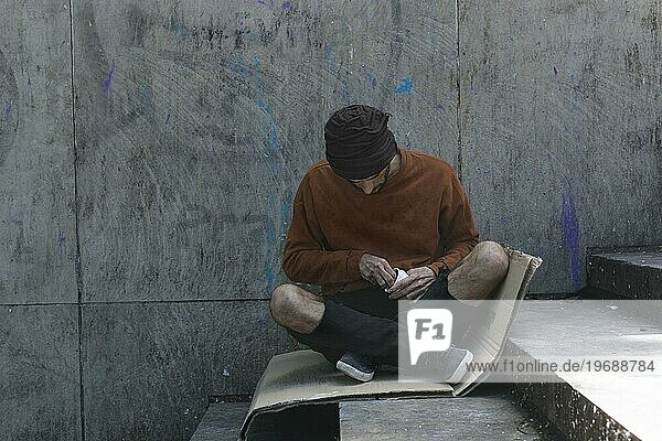 Obdachloser Mann sitzt im Freien auf einem Karton