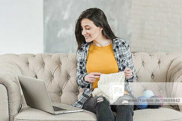 Frau strickend mit Blick auf Laptop