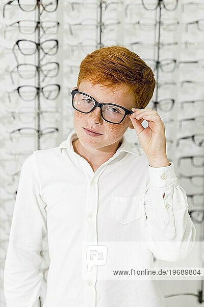 Unschuldiger Junge mit schwarzem Brillengestell in einem Optikgeschäft