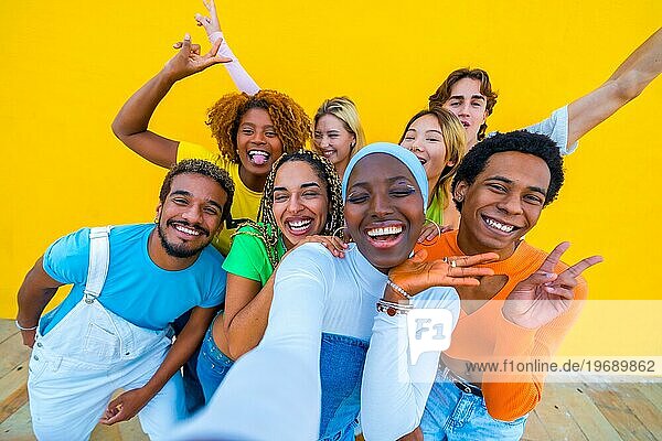 Frontalansicht einer multiethnischen Gruppe von Freunden  die fröhlich gestikulieren  während sie ein Selfie vor einem gelben Hintergrund machen