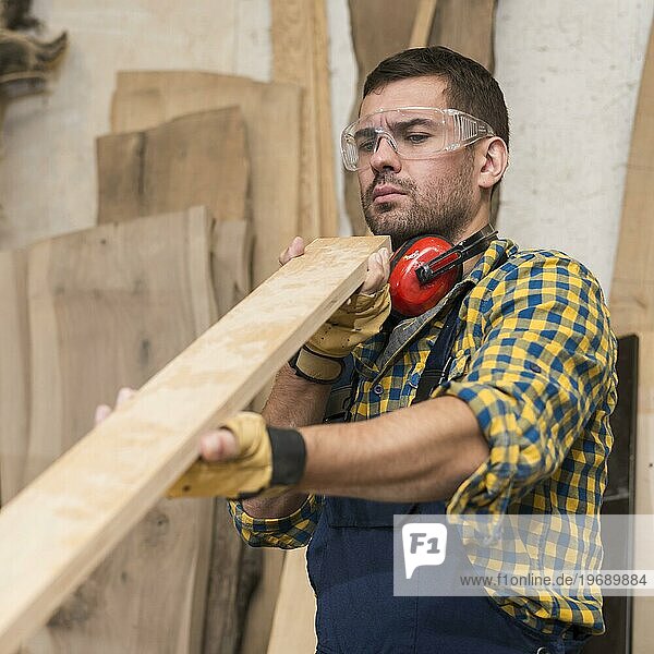 Männlicher Zimmermann  der ernsthaft nach einer Holzplanke sucht