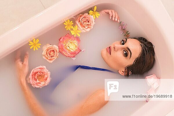 Künstlerisches Portrait von oben einer sinnlichen Frau  die ein Milchbad mit Blumen nimmt