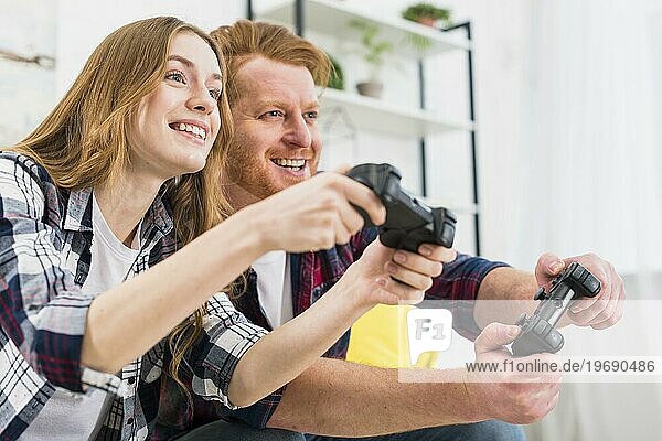Glückliches Portrait eines jungen Paares beim Spielen einer Spielkonsole mit Joysticks