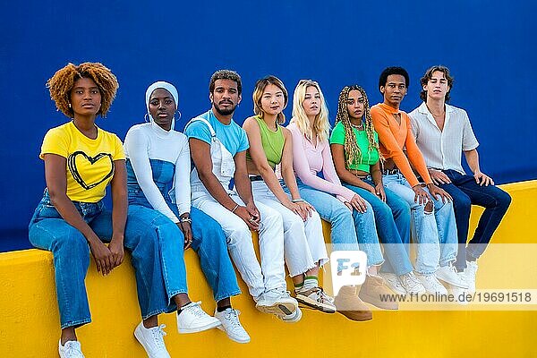 Seriöse Gruppe multiethnischer junger Menschen  die auf einer bunten Wand sitzen und in die Kamera schauen
