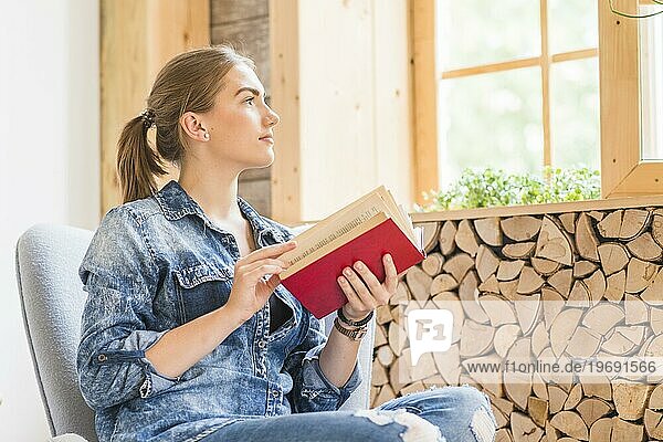 Attraktive junge Frau schaut zum Fenster und hält ein Buch