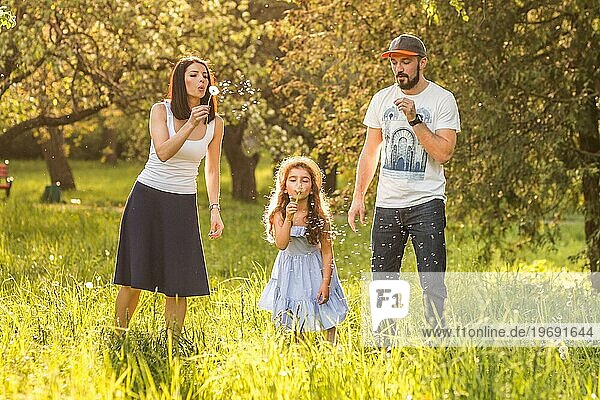 Tochter bläst Löwenzahn mit ihren Eltern