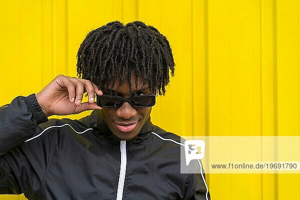 Afroamerikanischer junger Mann mit Sonnenbrille und cooler Einstellung neben einer gelben Stadtmauer
