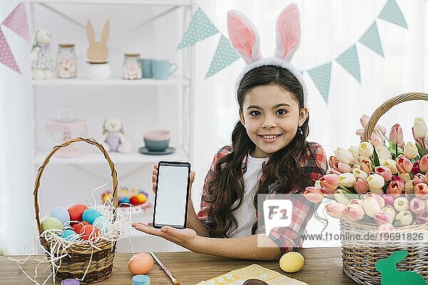 Glückliches Mädchen zeigt Handy mit Ostereiern Tulpen Korb Tisch