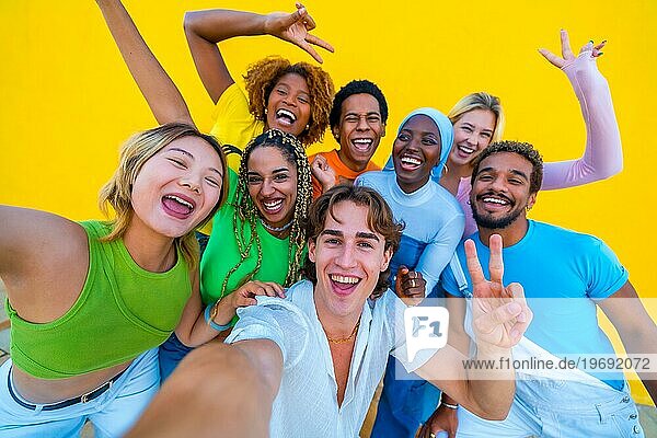 Junge Menschen verschiedener Ethnien machen ein fröhliches Selfie bei einer Versammlung vor einem gelben Hintergrund
