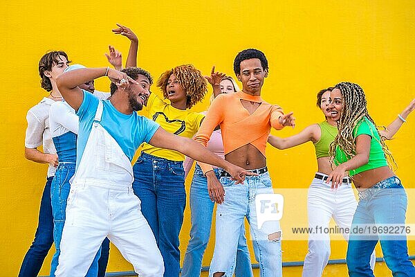 Multikulturelle Gruppe fröhlicher junger Menschen  die in einem gelben städtischen Raum zusammen tanzen
