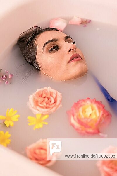 Künstlerisches Porträt von oben eines entspannten Modells  das ein Milchbad mit Blumen nimmt