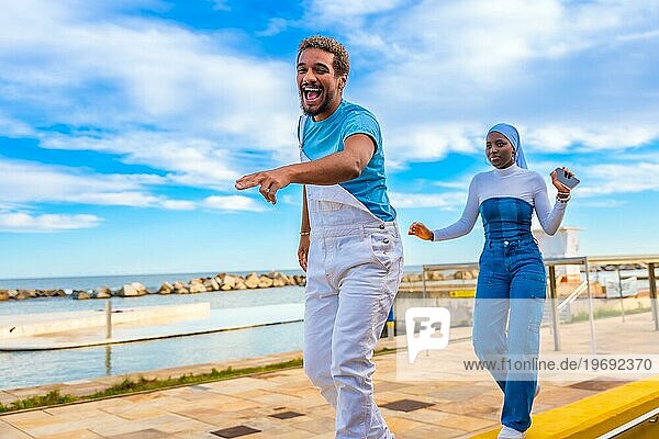Seitenansicht von zwei glücklichen multiethnischen Freunden  die am Meer tanzen