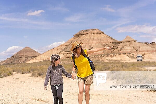 Horizontale Frontalansicht einer Mutter und einer Tochter  die sich an den Händen halten und in einem trockenen Nationalpark spazieren gehen
