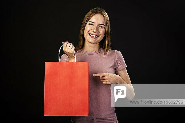 Vorderansicht glückliche Frau  die auf ihre rote Einkaufstasche zeigt