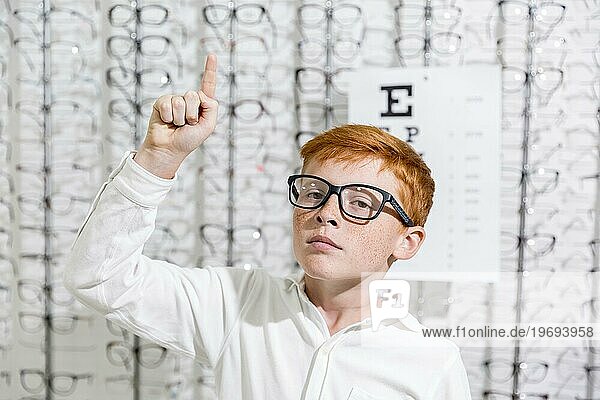Junge mit Brille zeigt nach oben Richtung stehen gegen Brillen Display Hintergrund