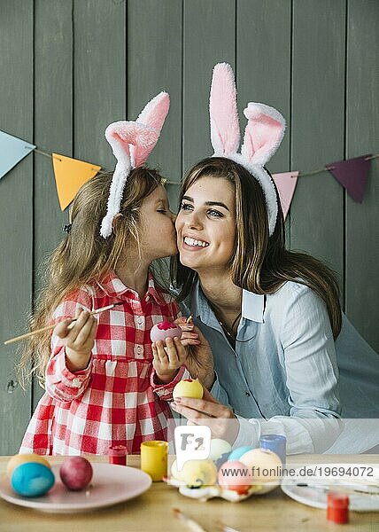 Nettes Mädchen küsst Mutter Wange während Malerei Eier Ostern