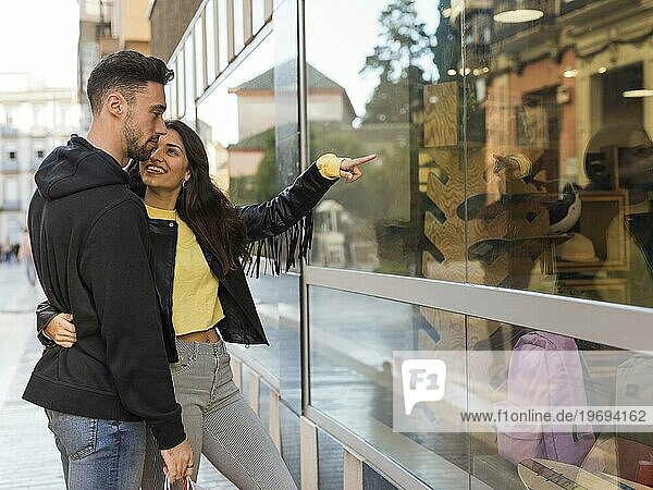 Happy woman hugging showing shop window young man