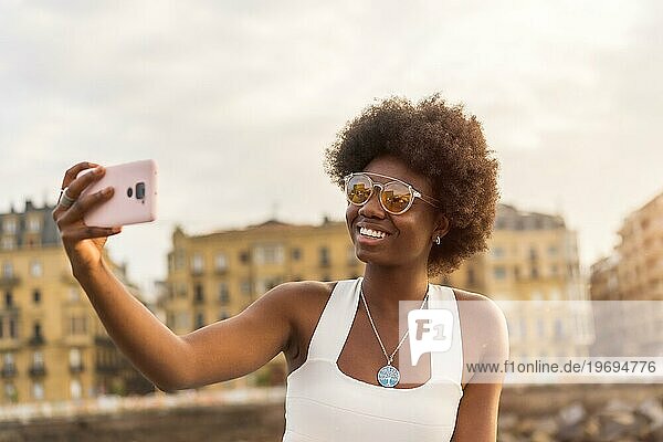Afrikanische junge Frau macht ein Selfie auf einer Promenade bei Sonnenuntergang
