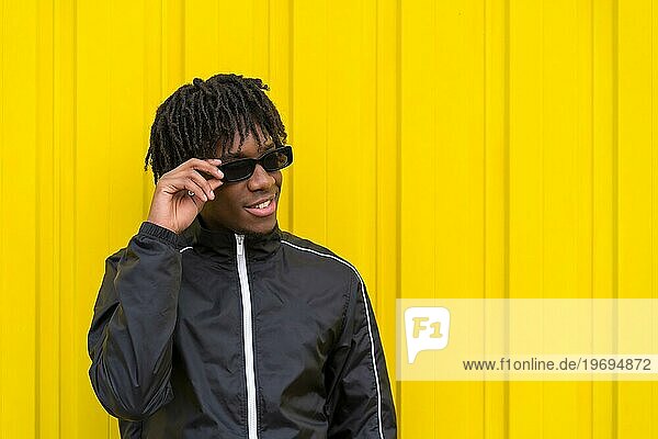 Afrikanischer junger Mann mit Sonnenbrille und cooler Einstellung neben einer gelben Stadtmauer