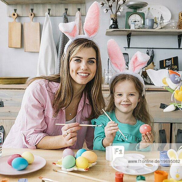 Glückliches Mädchen mit Mutter malt Eier Ostern