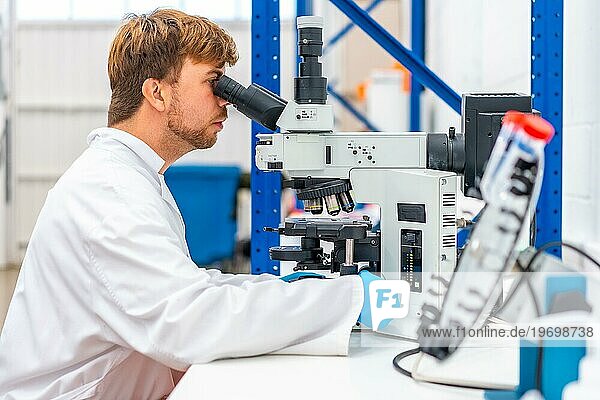Seitenansicht eines jungen  kaukasischen Wissenschaftlers  der in ein Mikroskop schaut  das auf einem Labor steht