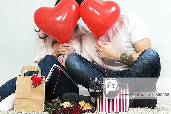 Paar bedeckt Gesichter mit roten Herzluftballons