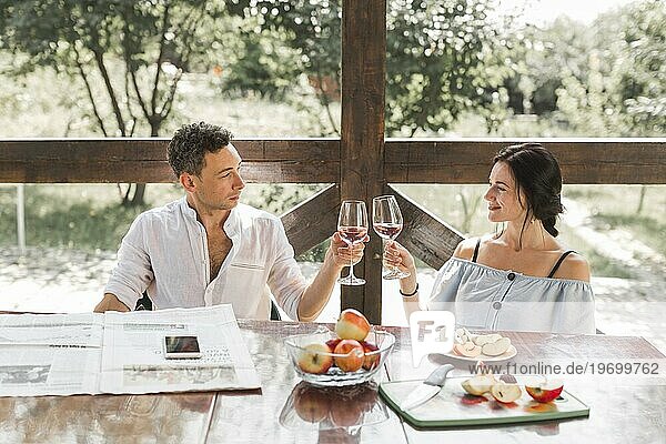 Lächelndes junges Paar stößt mit Weingläsern und Apfelfrüchten auf dem Tisch an