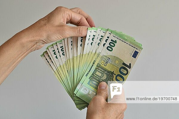 Eine Hand zählt viele einhundert Euro Geldscheine aufgefächert wie bei einem Kartenspiel  Symbolbild für Euro  Bargeld oder Reichtum