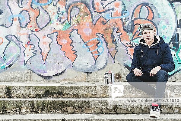 Mann sitzt vor Graffitiwand