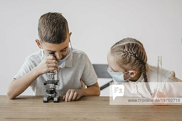 Kind mit medizinischer Maske schaut durch ein Mikroskop