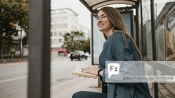 Frau wartet auf Bus und hält Buch